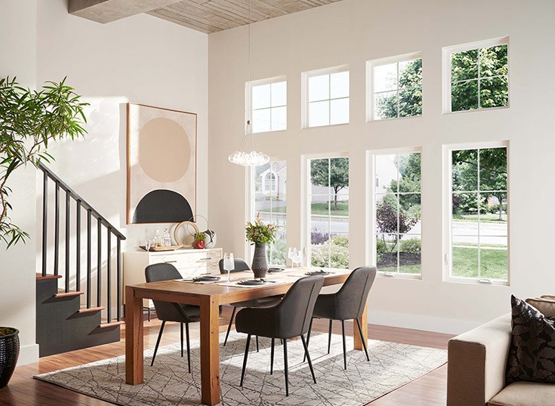A classic dining room with white Milgard Style Line windows and colonial grids. There are 4 tall windows in a row, and 4 small square windows above them. 