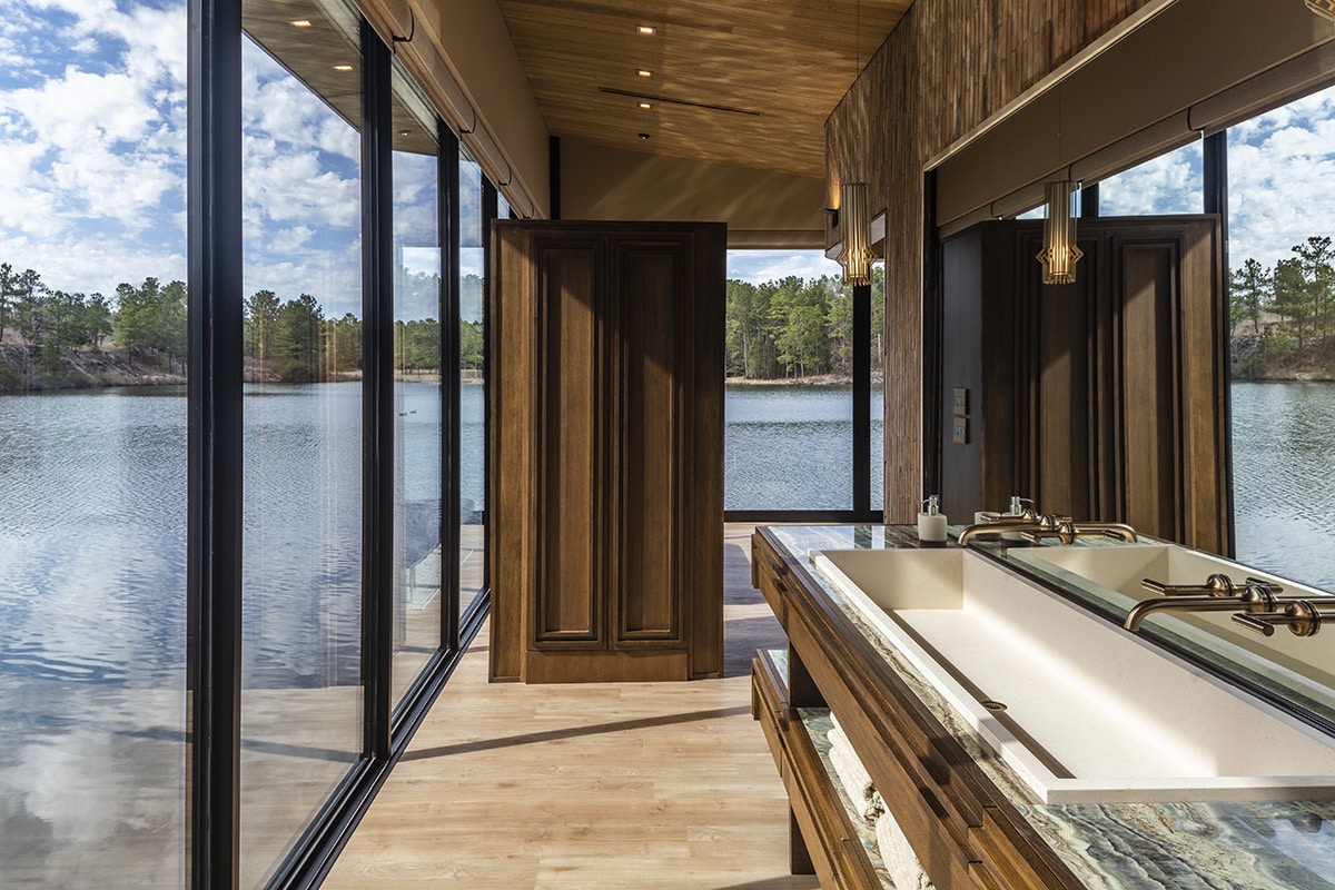 Photo from inside the bathroom of a house floating on a lake. The windows touch the floor and nearly reach the ceiling. The alignment of the mirror makes it look as if the house is incredibly narrow and has lake on both sides, but past the mirror the wall continues and there is a corner to the right. 