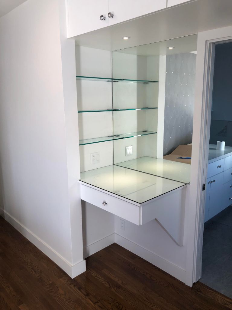 Corner vanity station for bathroom with mirror and glass shelves.