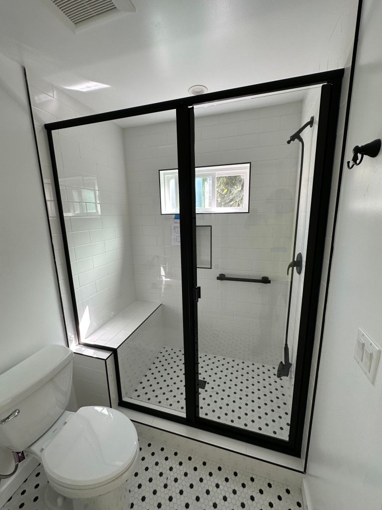Custom cut glass shower with black metal frame and a swinging pull door.